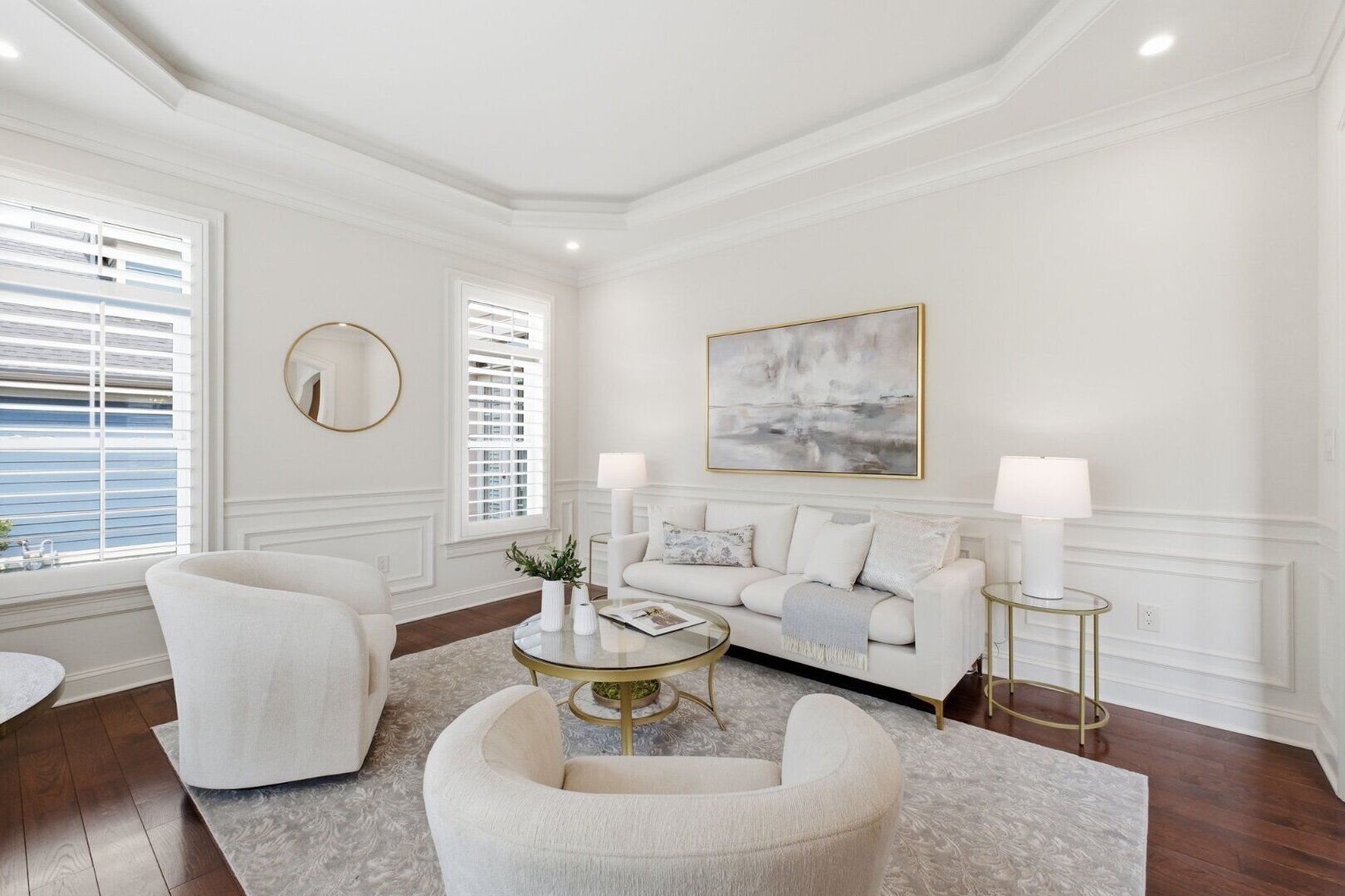 A crisp, elegantly staged living room with a cream sofa, curved accent chairs and a round brass coffee table